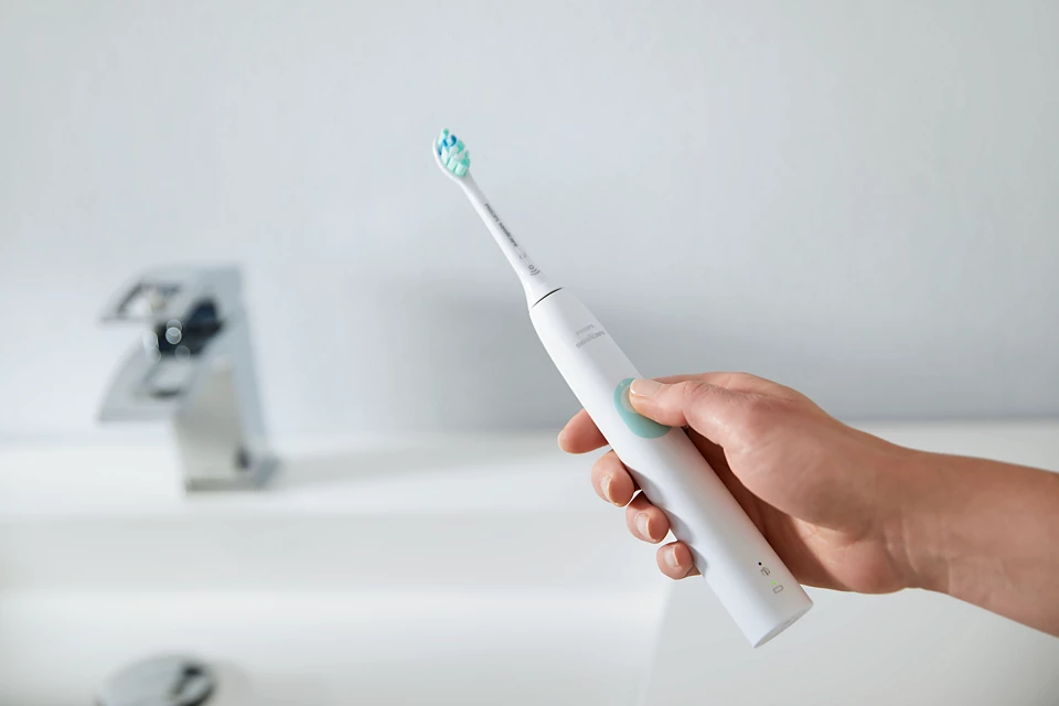 Hand holding a white Philips Sonicare electric toothbrush in a modern bathroom.